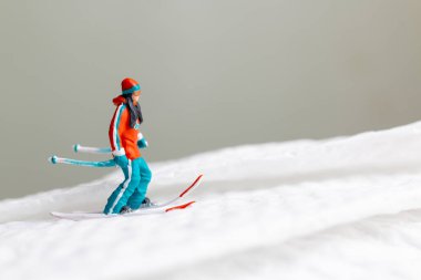 Canlı kış kıyafetleri giymiş minyatür bir kayakçı figürü. Kayakçı beyaz karlı bir arazide kayak yaparken yakalandı.