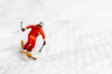 Canlı kış kıyafetleri giymiş minyatür bir kayakçı figürü. Kayakçı beyaz karlı bir arazide kayak yaparken yakalandı.