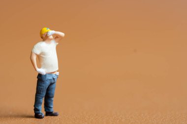 Minyatür insanlar, inşaat işçisi. Alnından ter silerken bir eli kalçasında duruyor.