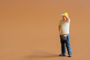 Minyatür insanlar, inşaat işçisi. Alnından ter silerken bir eli kalçasında duruyor.