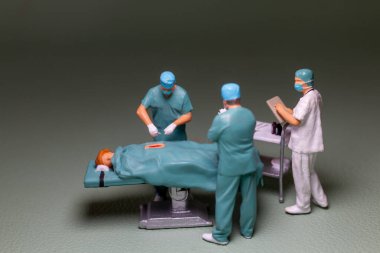 Minyatür insanlar, tıbbi personel cerrahi sahnesi devam ediyor figürler önlük, yüz maskesi ve kep giyecek, tipik bir ameliyathane ortamı..
