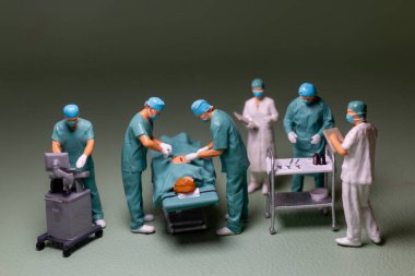 Minyatür insanlar, tıbbi personel cerrahi sahnesi devam ediyor figürler önlük, yüz maskesi ve kep giyecek, tipik bir ameliyathane ortamı..