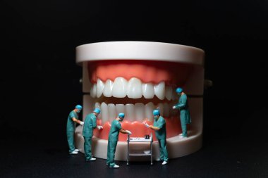 Cerrahların minyatür heykelcikleri insan dişlerinin büyük bir modeli üzerinde çalışıyorlar..