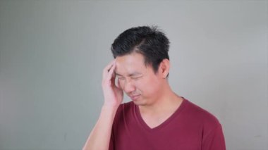 Kestane rengi gömlekli bir adam gözleri kapalı bir şekilde başını tutuyor. Ağrı ya da rahatsızlık belirtileri gösteriyor. Baş ağrısı ya da migren olabilir.. 