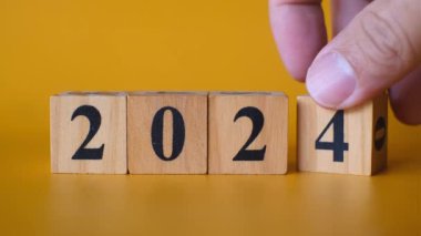 Ahşap blokları siyah sayılarla ayarlayan bir elin yakın çekimi 2025 'i canlı sarı bir arka plana karşı oluşturur.