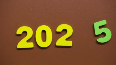 Kahverengi desenli arka planda sıralanmış sarı ve yeşil parmaklı 2025 renkli sayılarını gösteren hareket dizisini durdur