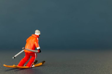 Kayakçının minyatür figürü, koyu bulanık bir arkaplan üzerine kurulmuş canlı renklerle detaylandırılır, kış sporları temaları için mükemmeldir.