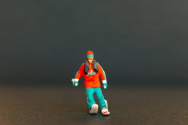 Kayakçının minyatür figürü, koyu bulanık bir arkaplan üzerine kurulmuş canlı renklerle detaylandırılır, kış sporları temaları için mükemmeldir.