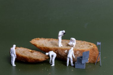 Adli tıp müfettişi gibi giyinmiş minyatür heykelcikler ekmek dilimlerini ekipmanla inceliyorlar. Olay yeri incelemesini yemek temalarıyla harmanlayan yaratıcı ve ilginç bir kavram.