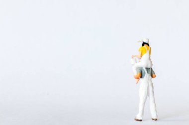 Kızını beyaz arka planda omuzlarında taşıyan bir babayı gösteren büyüleyici bir minyatür sahnenin yakın çekimi.