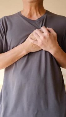Gri gömlekli bir adam iki elini göğsüne bastırıyor. Ağrı veya rahatsızlık veriyor..