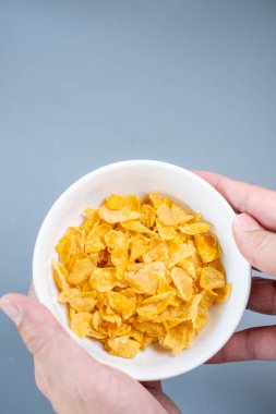 Minimalist gri arka planda gevrek altın mısır gevreğiyle dolu beyaz bir kase. Kahvaltı, sağlıklı beslenme ve yemekle ilgili kavramlar için mükemmel..