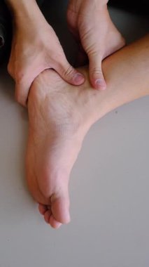 Ayak bileğine masaj yapan, acıyı ve gerilimi azaltmak için baskı uygulayan ellerin yakın çekimi..