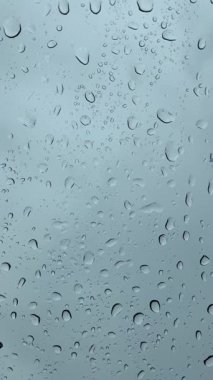 Arkasında yumuşak mavi bir gökyüzü olan cam bir yüzeye saçılmış temiz su damlacıkları. Sakin, minimalist bir çekim. Arka plan için ideal.