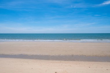 Tayland 'daki Cha-am Sahili, temiz kumlu bir kıyı şeridi, yumuşak dalgalar ve açık mavi bir gökyüzü.
