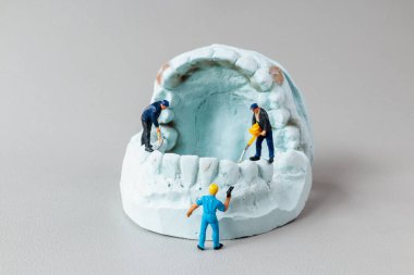 Yaratıcı konsept görüntüsü, diş macunu modelini temizleyen inşaat işçilerinin minicik heykellerini gösteriyor.