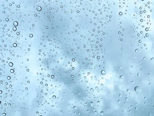 Camdaki yağmur damlaları karanlık, bulutlu gökyüzüne karşı barışçıl ve atmosferik