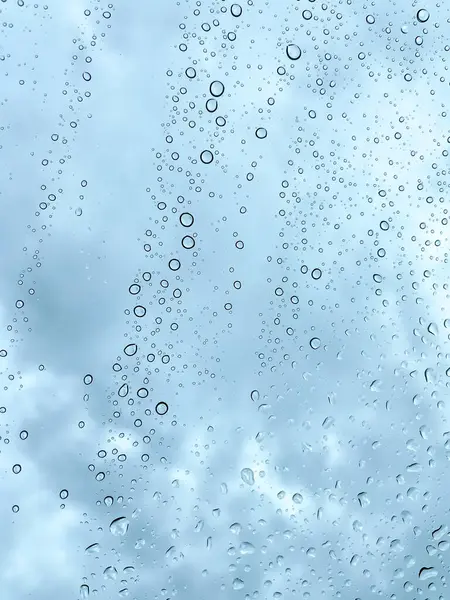 Camdaki yağmur damlaları karanlık, bulutlu gökyüzüne karşı barışçıl ve atmosferik