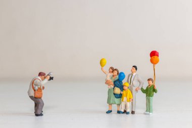 Elinde renkli balonlar tutarken fotoğraf için poz veren bir ailenin minyatür figürlerinin yer aldığı sevimli kavramsal görüntü.