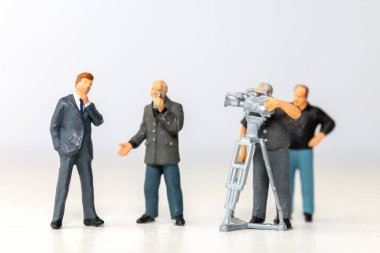 Bir erkek gazetecinin minyatür figürü bir kameraman kaydıyla bir iş adamıyla röportaj yapıyor. Bu sahne gazetecilik ve iş dünyasındaki iletişim sürecini temsil ediyor.