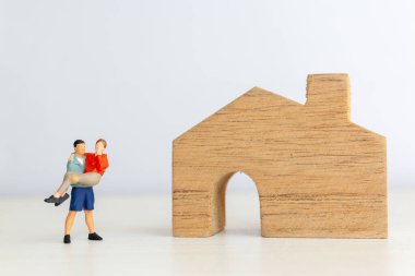 Minyatür bir adamın, tahta bir ev figürünün yanında bir kadını kollarında taşıdığı garip kavramsal tasviri.