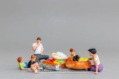 Minyatür heykelciklerin, büyük boy tatlı ve meyveli hamur işlerinde pikniğin keyfini çıkardığı tuhaf bir sahne.