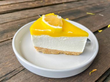 Taze limonlu cheesecake dilimine yakın plan beyaz tabakta, ahşap masanın üzerinde.