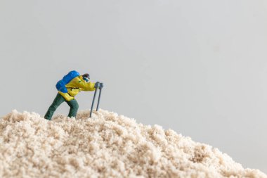 Sırt çantası ve direkleri olan, macera ve keşfi temsil eden kum tepesine tırmanan küçük bir yürüyüş figürünün yakın çekimi.