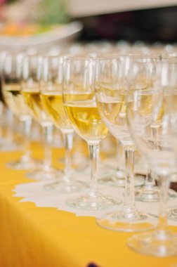 Many wine glasses in rows on a table with a yellow tablecloth. Glasses filled with red wine and white wine. Restaurant setting or an event like drink or wine tasting, blurry bokeh background.