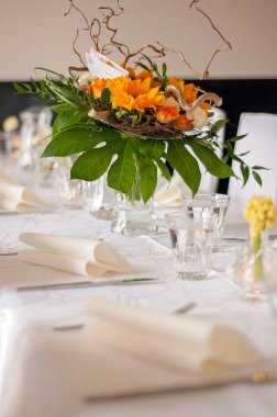 Beautiful set table with a white tablecloth and tableware like cutlery, glasses and napkins. Big flower arrangement in a glass vase. Restaurant, event or wedding setting and no people.