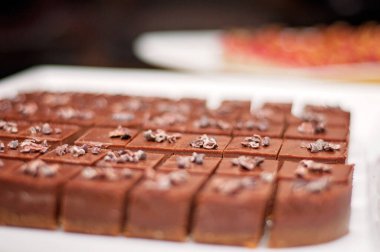 Many small chocolate desserts on a white dish. Chocolate mousse cakes decorated with chocolate flakes or nuts. 