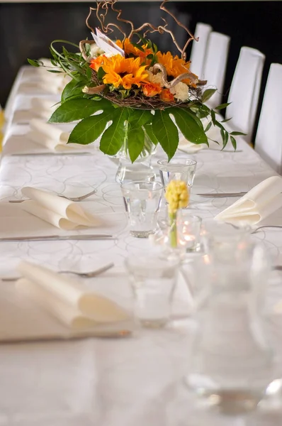 Beautiful set table with a white tablecloth and tableware like cutlery, glasses and napkins. Big flower arrangement in a glass vase. Restaurant, event or wedding setting and no people.