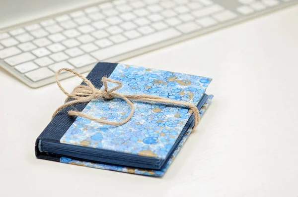 Blue unique notebook, book, journal, planner or calendar tied with brown string with a ribbon on a desk with a computer keyboard in the background. Desk at work, workspace.