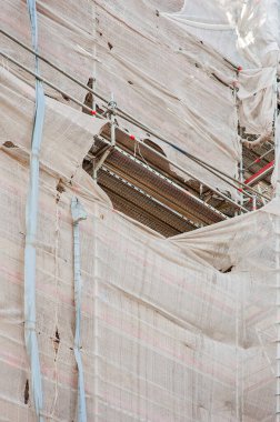 Worn and ripped sheet covering scaffolding in a construction site in Budapest, Hungary, Europe. Reconstructing and repairing a building, covered with scaffolding sheet. 
