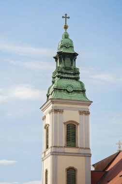 Budapest Inner City Parish Church or Church of the Blessed Virgin Mary tower, Hungary, Europe. White tower with green or blue roof and a cross on top against the blue cloudy sky.
