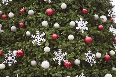 Close-up of a decorated Christmas tree outside. Evergreen tree decorated with red, white and silver ball ornaments, white snowflake ornaments and small Christmas lights. Budapest, Hungary, Europe.