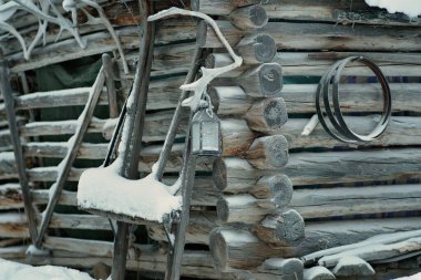 Old rustic houses made of timber and covered in snow. Some tools on the side of the wooden house. Snowy village in Lapland, Finland on a cold winter day.