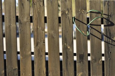 Old unpainted wooden fence on property. Traditional fence construction made to protect and secure. Green plastic wire hanging on plank.