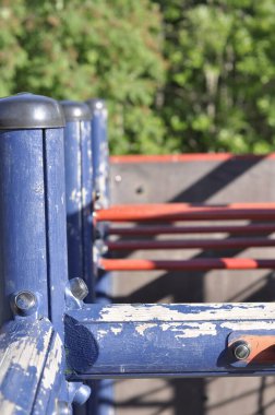 Close-up of a blue and red climbing frame or jungle gym in playground on a sunny summer day in sunlight. Sandy schoolyard with green trees and forest in the background.