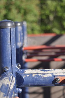Close-up of a blue and red climbing frame or jungle gym in playground on a sunny summer day in sunlight. Sandy schoolyard with green trees and forest in the background.