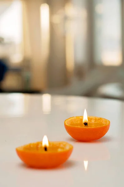 Romantic candles made of orange fruits and paraffin. Fruit candles in closeup on white table with blurred background.