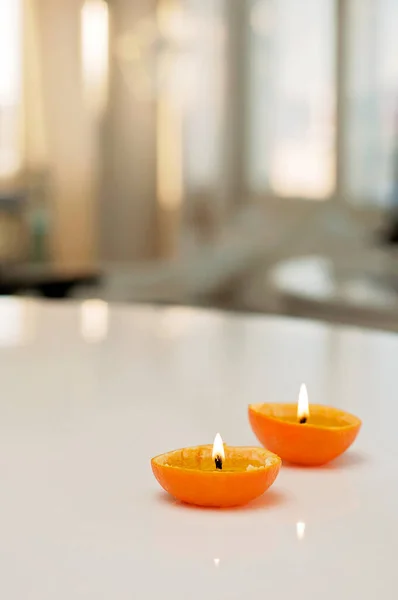 Romantic candles made of orange fruits and paraffin. Fruit candles in closeup on white table with blurred background.