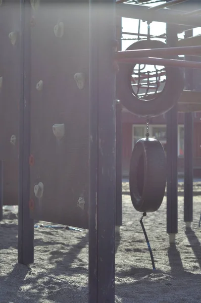 Playground with sand bed, climbing frame or jungle gym, climbing wall and tyre or tire swing. Schoolyard on a sunny and warm summer day, sunlight peaking through equipment.