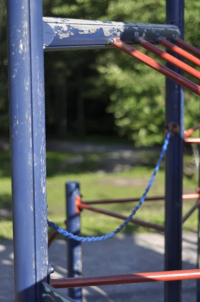 Close-up of a blue and red climbing frame or jungle gym in playground on a sunny summer day in sunlight. Sandy schoolyard with green trees and forest in the background.