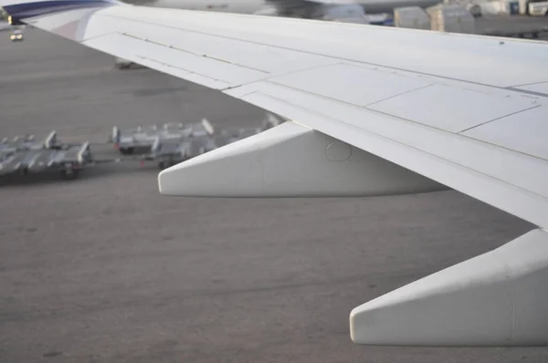Close-up of an airplane wing pictured from inside the aircraft. Plane landing or waiting to leave ground on the airport during morning or daytime.