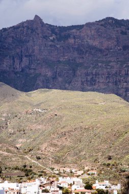 İspanya, Gran Canaria 'daki dağların ya da kayalık tepelerin çarpıcı manzarası. Dağlar arasında bir vadide birçok ev ve bina olan bir kasaba. Yürüyüş ve güzel doğa manzarası..