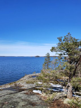 İlkbaharda deniz kenarındaki uçurumda hâlâ erimemiş biraz kar var. Gökyüzü ve deniz parlak mavi ve ufukta sadece birkaç bulut var. Fince takımada görünümü.
