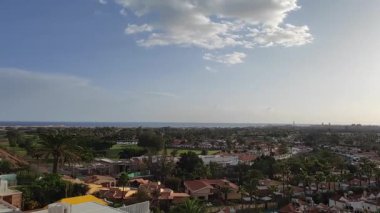 İspanya, Gran Canaria 'da tatil beldesi. Ufukta bir sürü evi, palmiye ağaçları ve okyanusu olan bir otel manzarası. Bulutlu mavi gökyüzü, güneş sıcacık parlıyor. Kanarya Adalarında Seyahat.