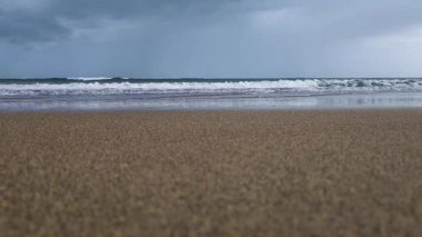 Sahilden denize bakıyorum. Dalgalar kıyıya çarpıyor, su ileri geri akıyor. Sakin dalgalar sahile vuruyor. Huzurlu, sakin ve sakin bir sahne, gökyüzü bulutlu.