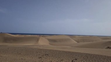 Maspalomas plajı ve Gran Canaria, İspanya 'daki sahil kum tepeleri. Çöl benzeri kum bölgesi, mavi gökyüzü ve güneş ışığı. Mavi okyanus ufukta görünüyor. Görünürde kimse yok, sadece sakin doğanın tadını çıkarıyoruz..